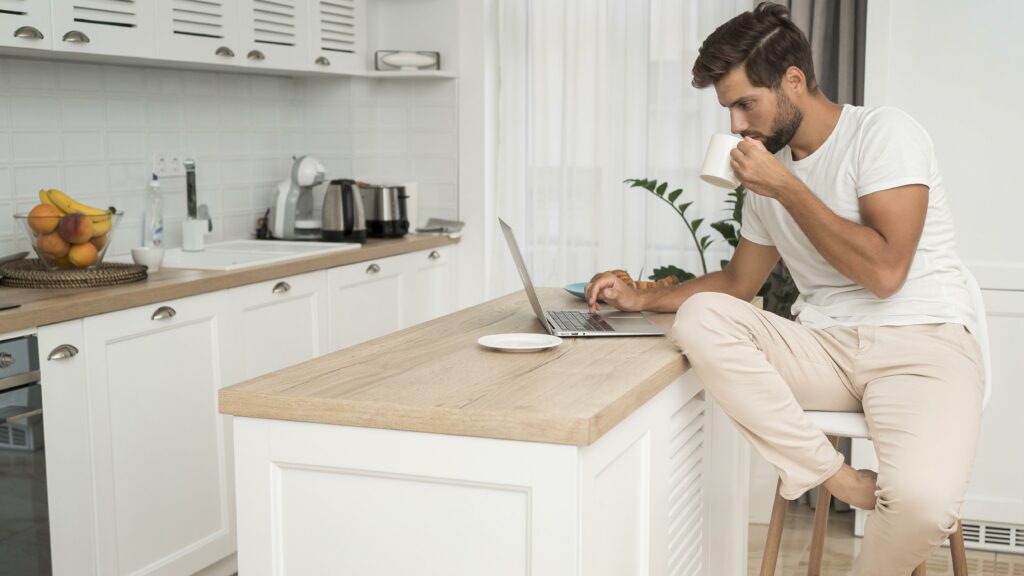 Man working remotely from his home kitchen while sipping coffee